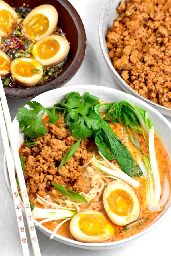 一碗粉色的汤，里面有碎猪肉、拉面、小白菜和溏心蛋。